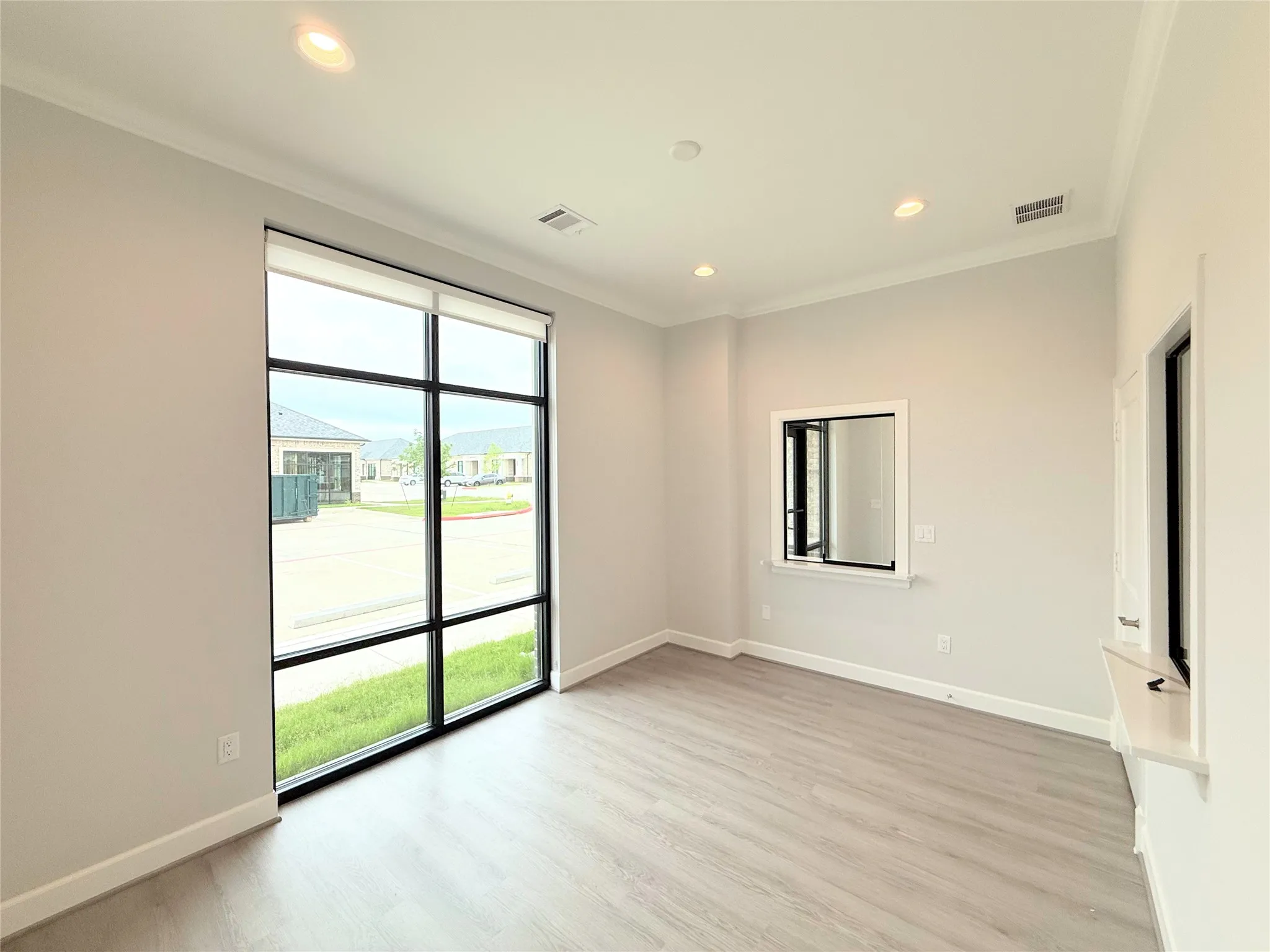 Spacious room featuring floor-to-ceiling windows, wood-finish flooring, recessed lighting, and crown molding