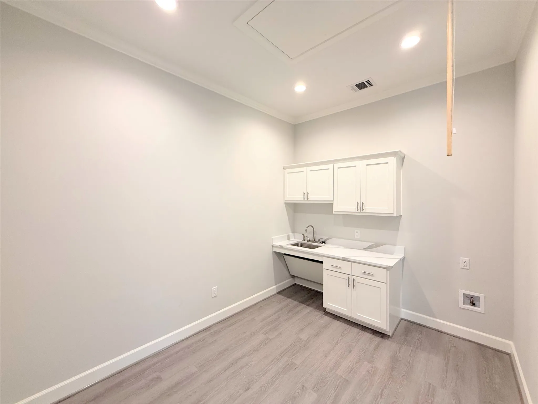 Utility area featuring white cabinetry, a stainless steel sink, light-toned countertops, and wood-finish flooring