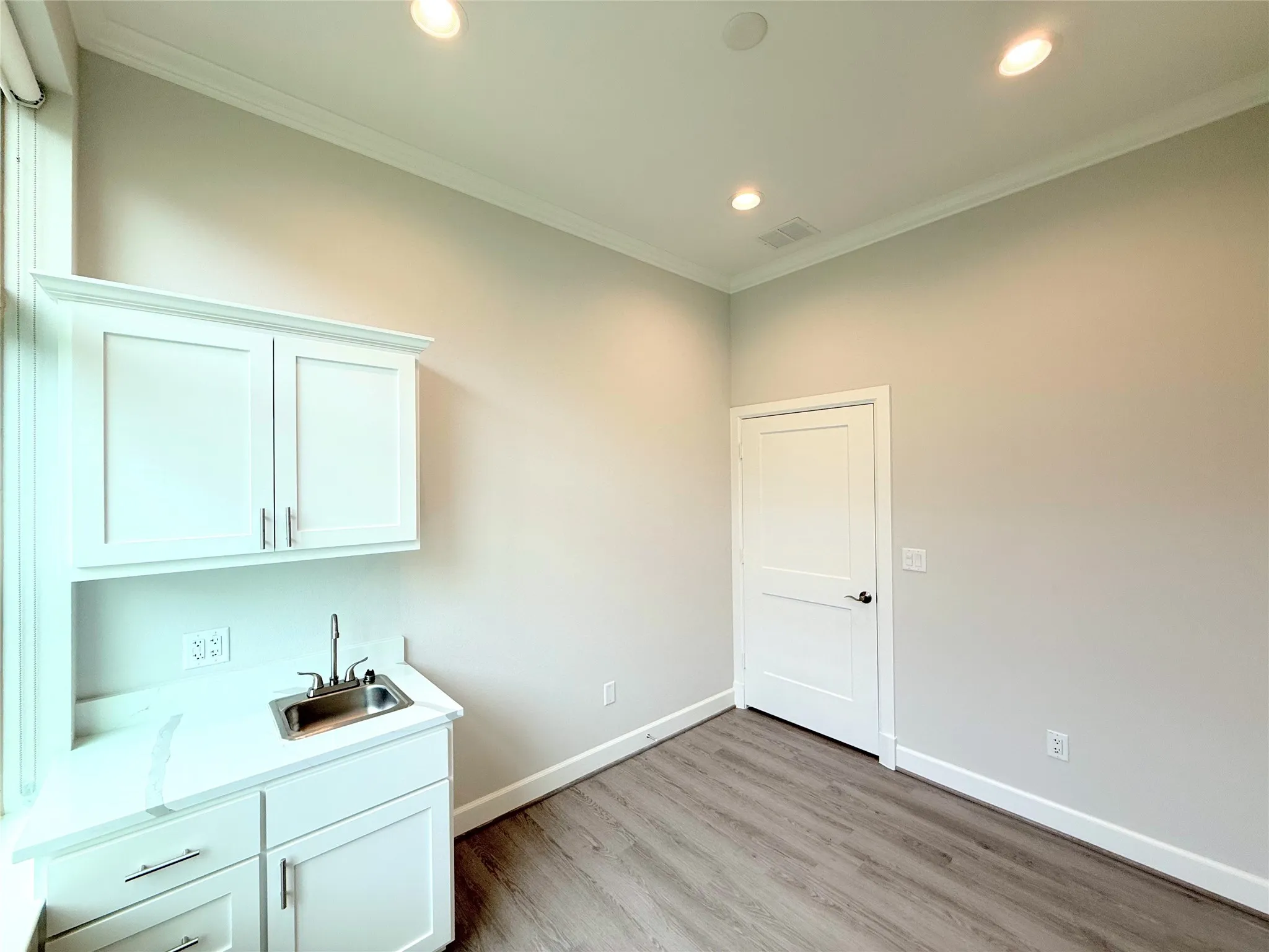 Utility room featuring white cabinetry, a stainless steel sink, light-toned countertops, and wood-finish flooring