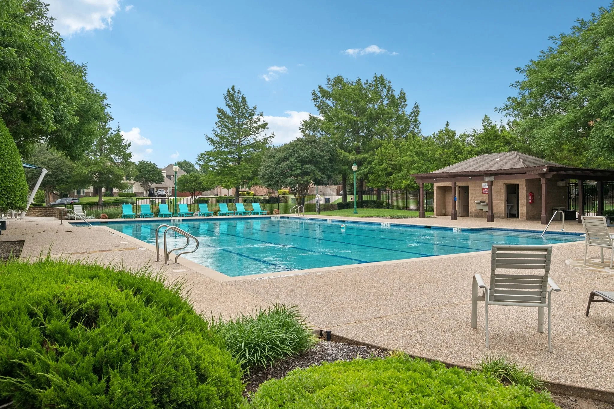 Resort-style pool area featuring a perimeter of mature trees, an adjacent covered pavilion, and a stone-finish pool deck