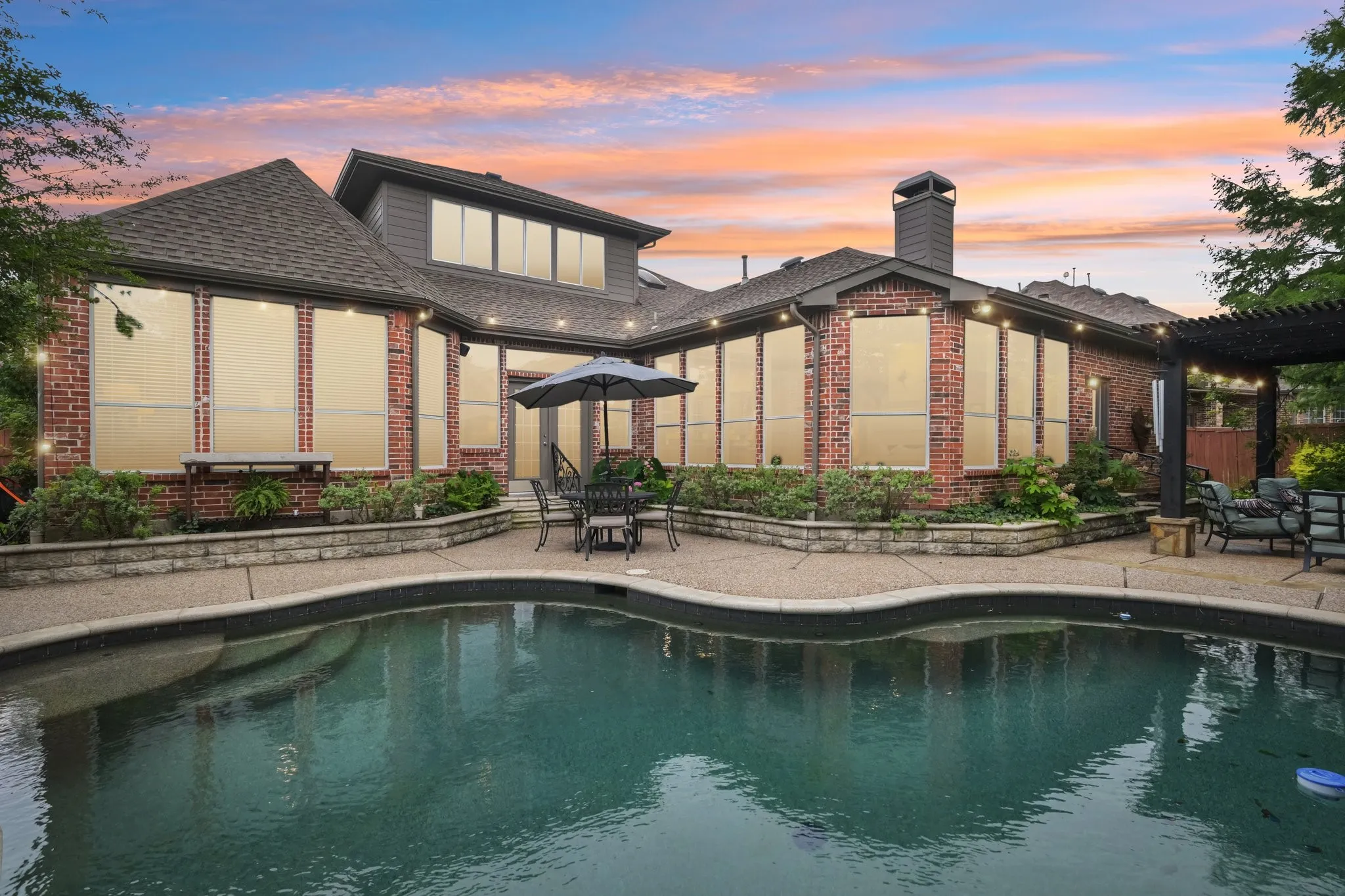 Backyard oasis featuring a swimming pool with integrated steps, an expansive concrete patio, and a brick exterior home with numerous large windows
