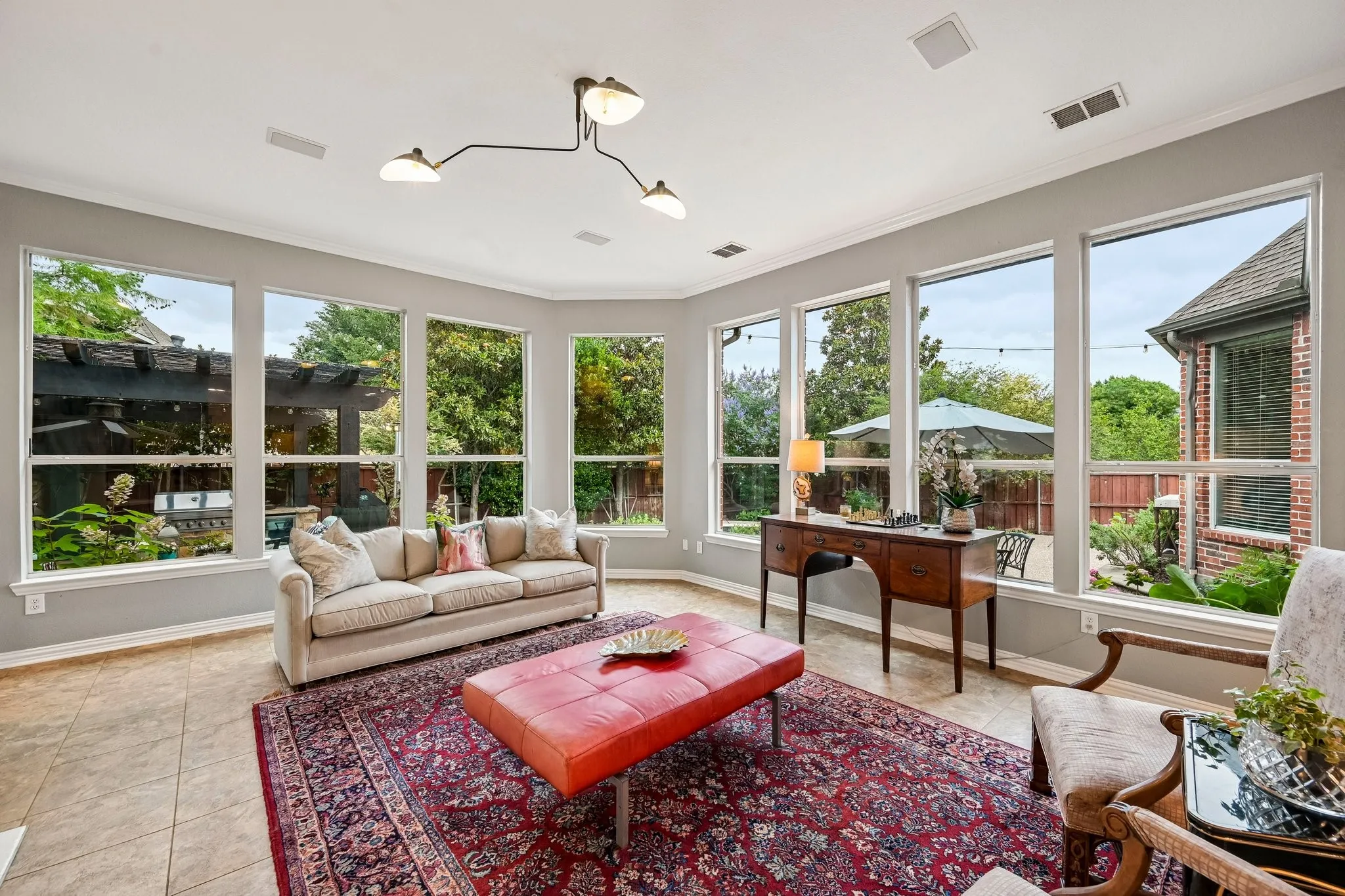 Sunlit living area featuring extensive window-lined walls, a contemporary multi-arm ceiling fixture, crown molding, and tiled flooring