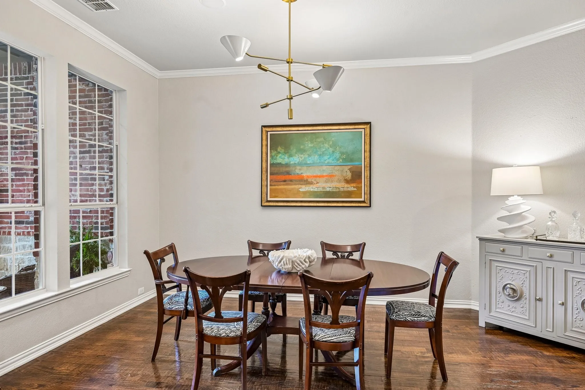 Dining space featuring wood-finish flooring, a contemporary chandelier, two large windows with mullions, and crown molding