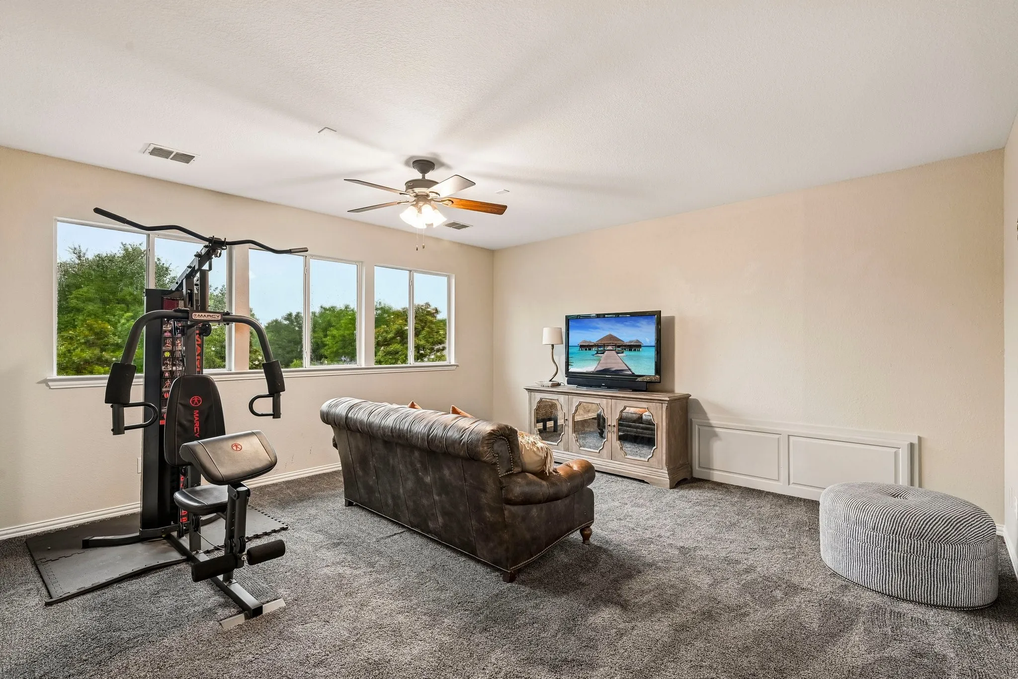 Carpeted room featuring a ceiling fan, multiple windows with exterior views, and built-in white paneling