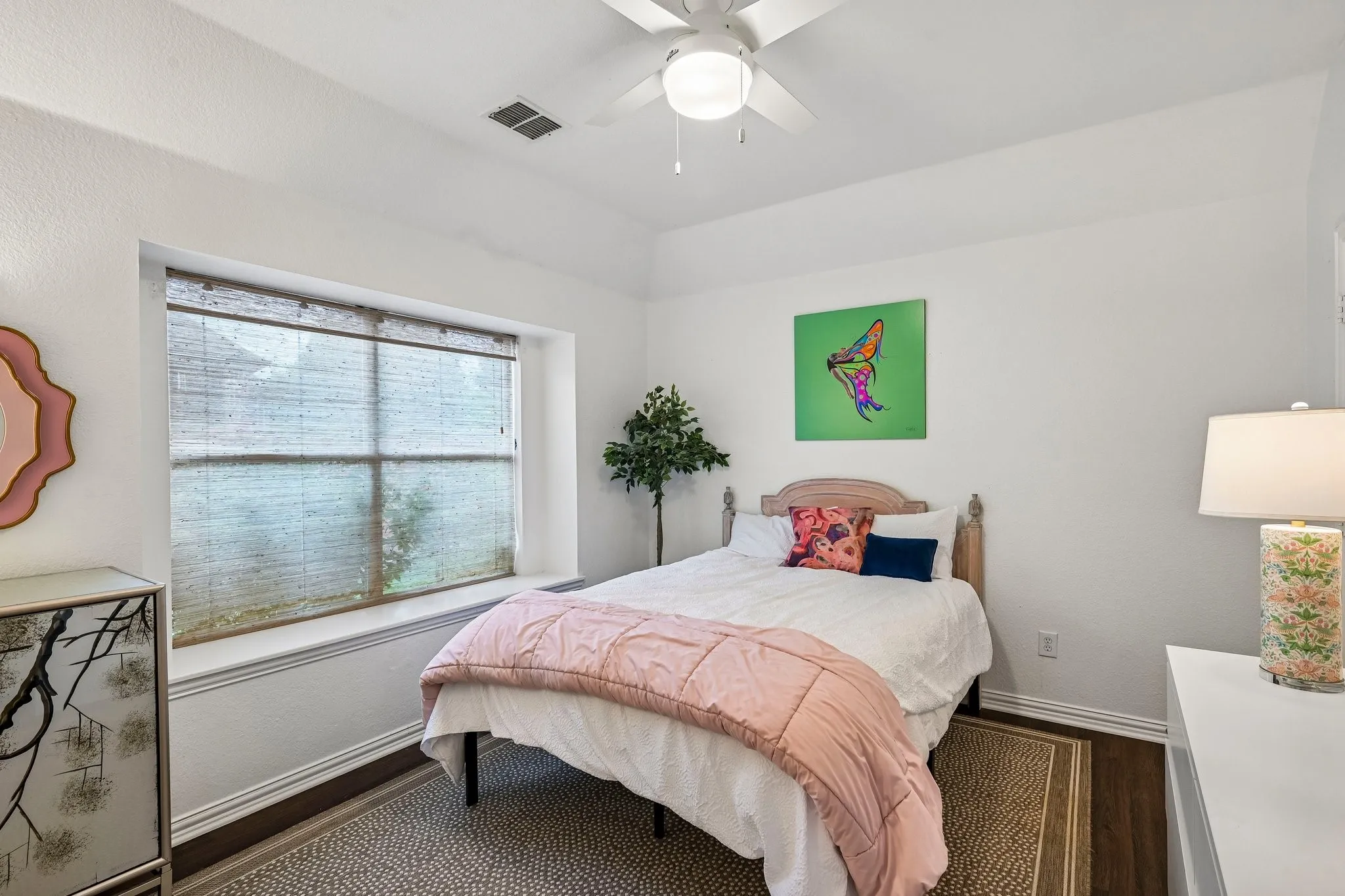 Bedroom featuring a bay window with natural light, wood-finish flooring, a ceiling fan, and white walls