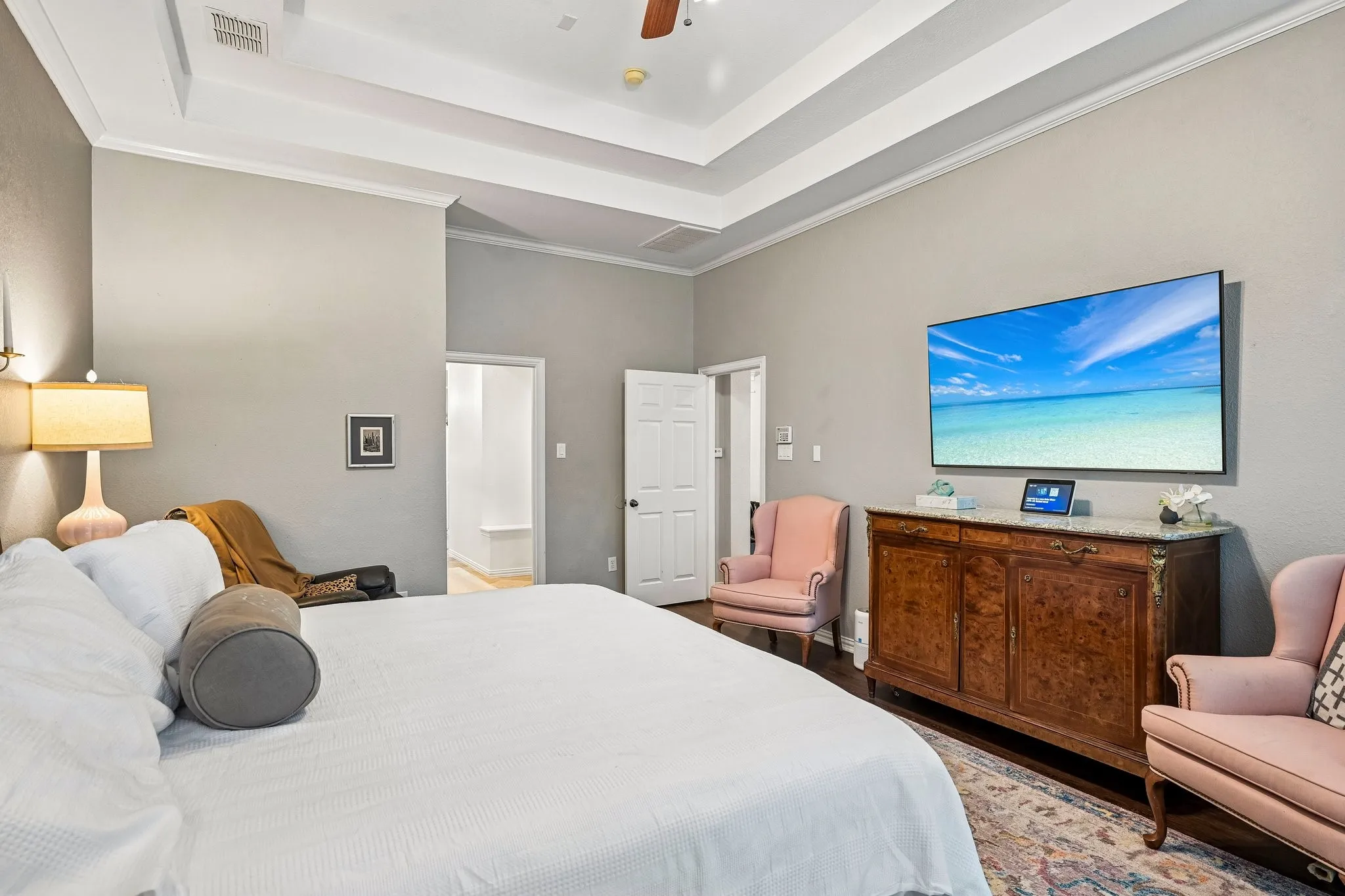 Spacious room featuring a tray ceiling with crown molding, light gray wall tones, and a dark wood-finish flooring