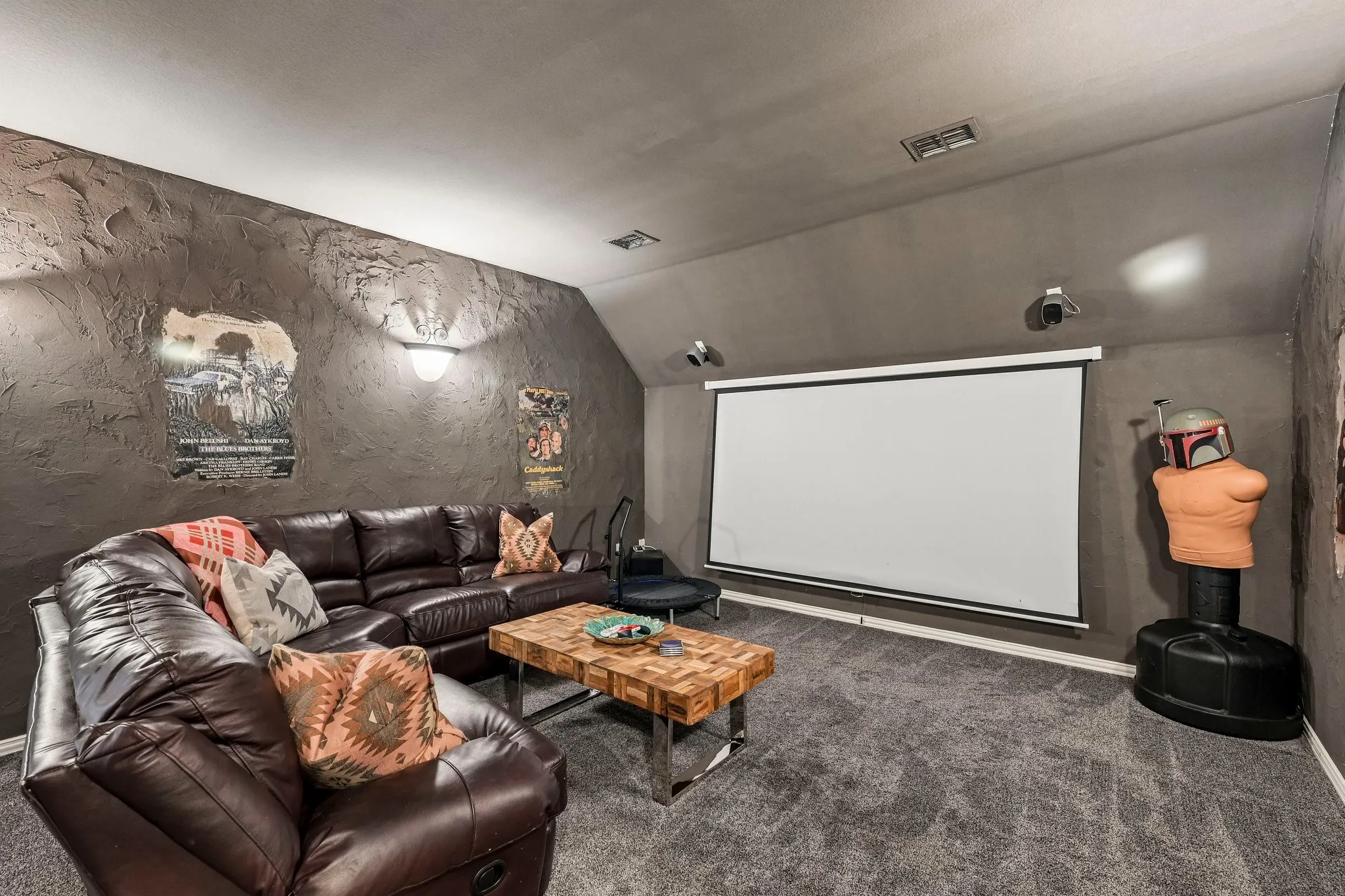 Dedicated media room featuring a large projector screen, wall-mounted speakers, recessed lighting, and textured wall finishes