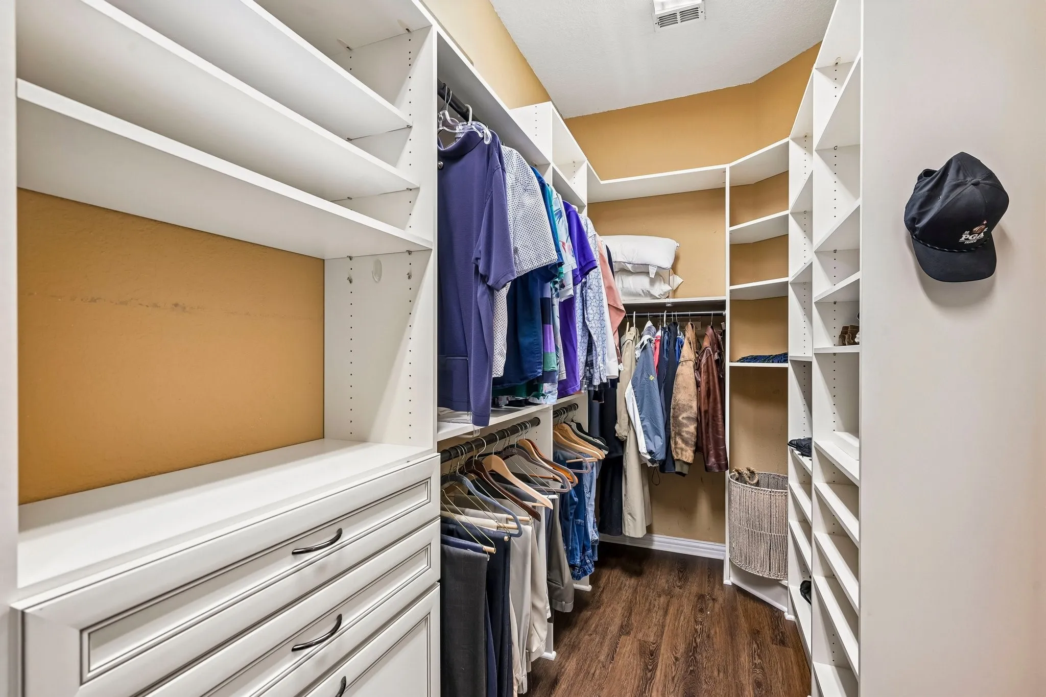 Walk-in closet featuring white built-in shelving, hanging rods, multiple drawers, and wood-finish flooring