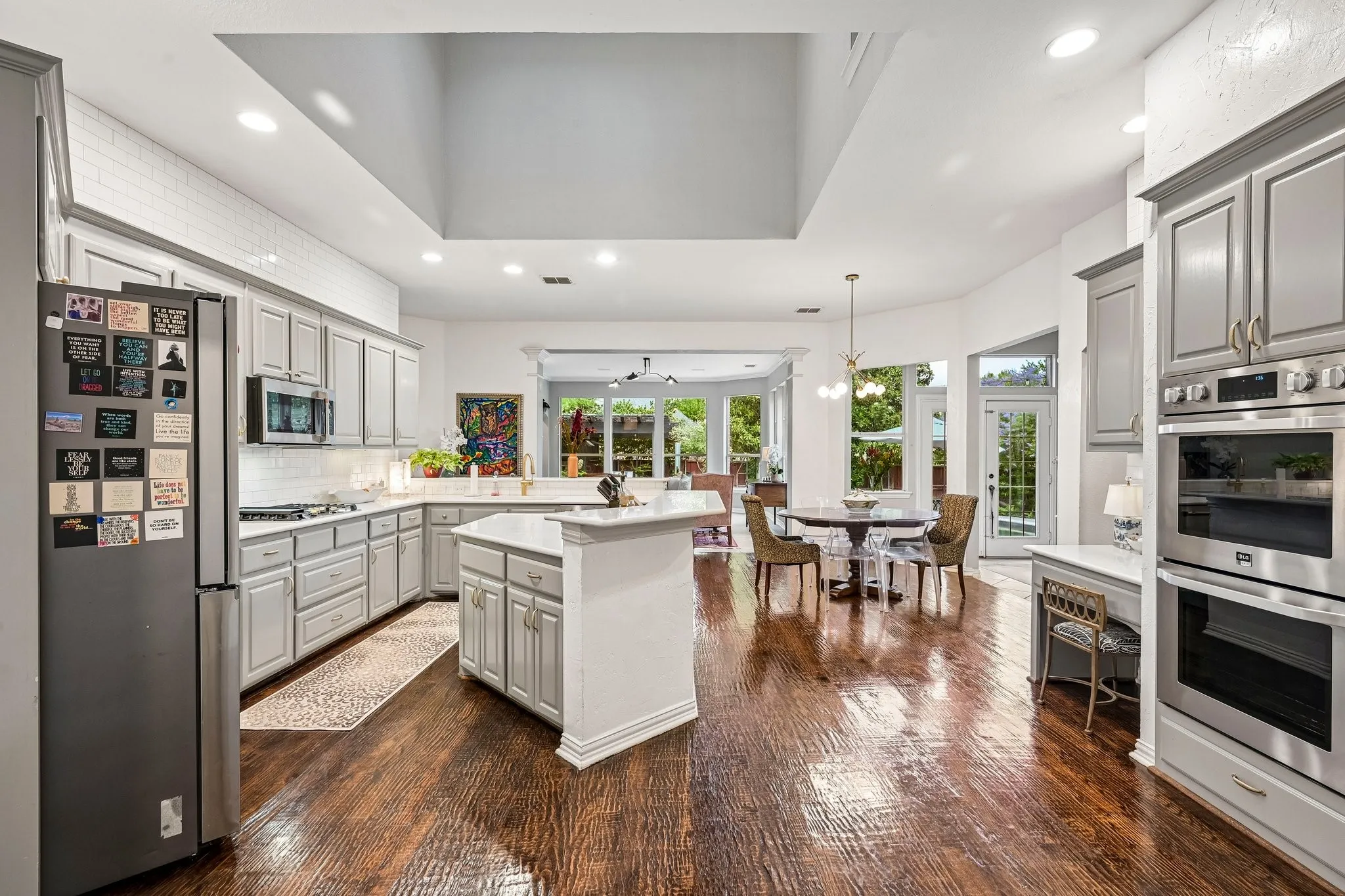 Spacious kitchen featuring wood-finish flooring, light gray cabinetry, a central island with a solid surface countertop, stainless steel appliances, and subway tile backsplash
