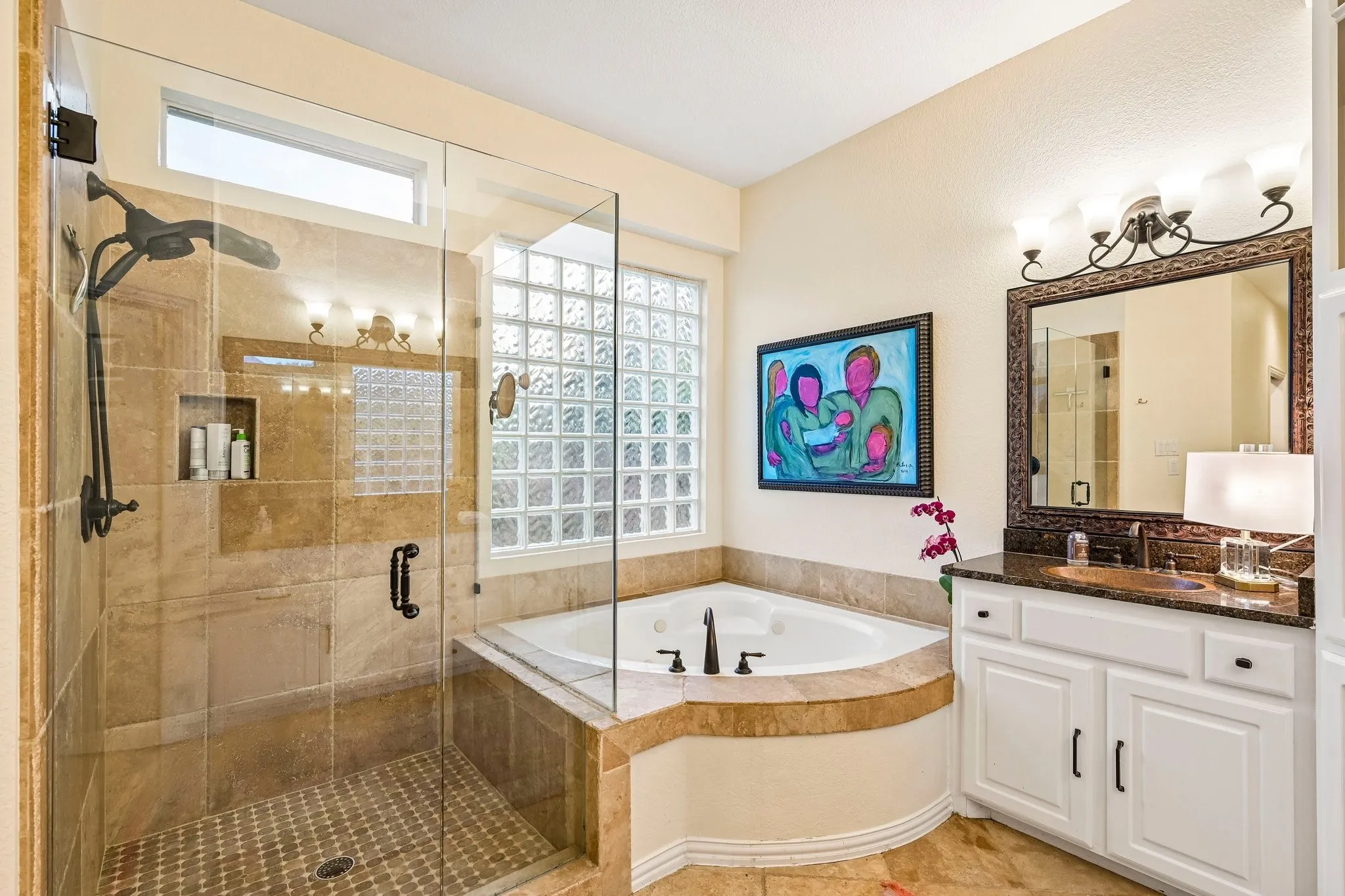 Bathroom featuring a glass-enclosed shower with stone tile, a built-in corner tub with stone surround, a vanity with a dark countertop and white cabinetry, and a glass block window
