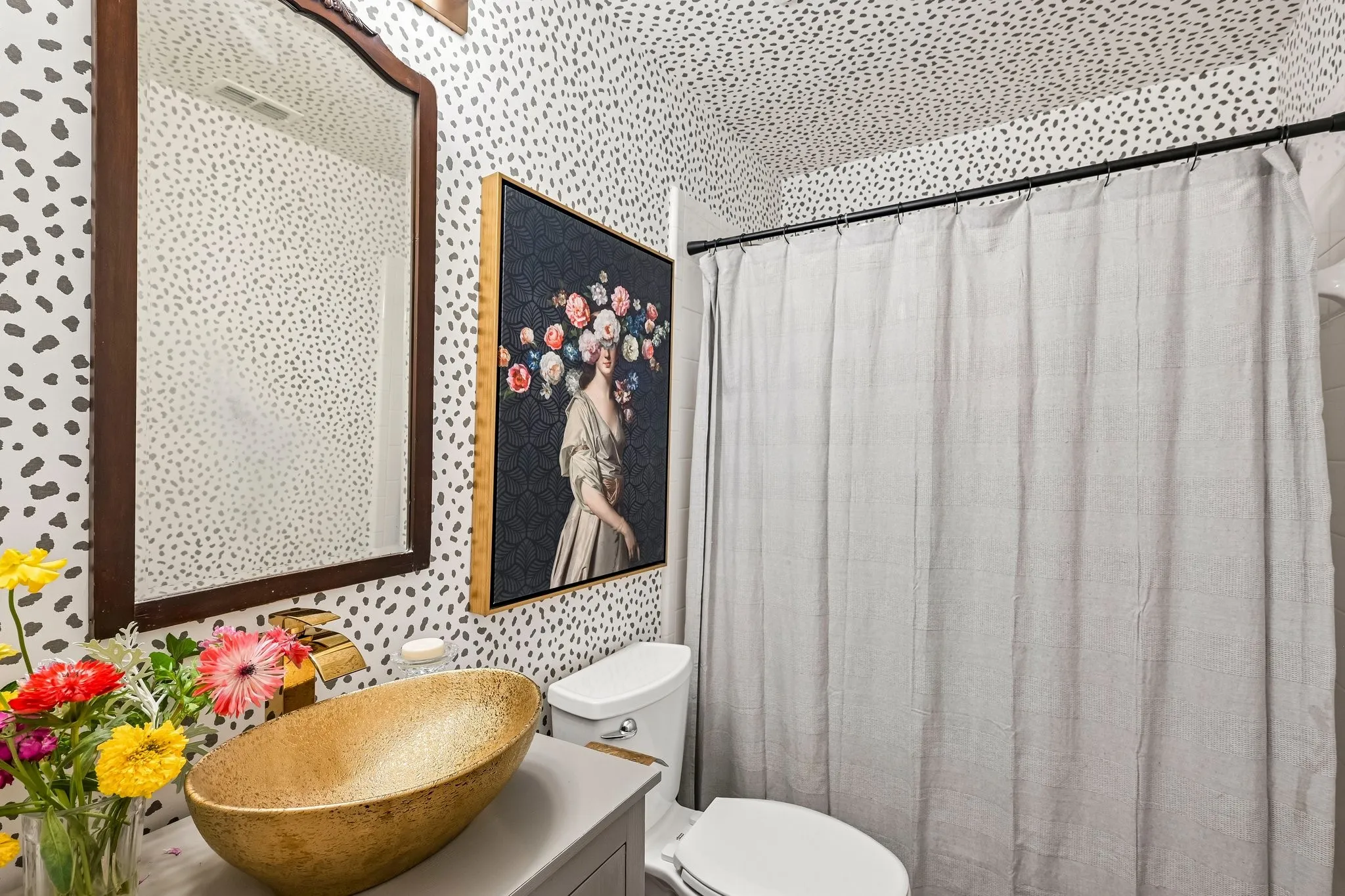 Bathroom featuring a vessel sink with a gold-tone faucet, a dark wood-framed mirror, and a wall-mounted toilet