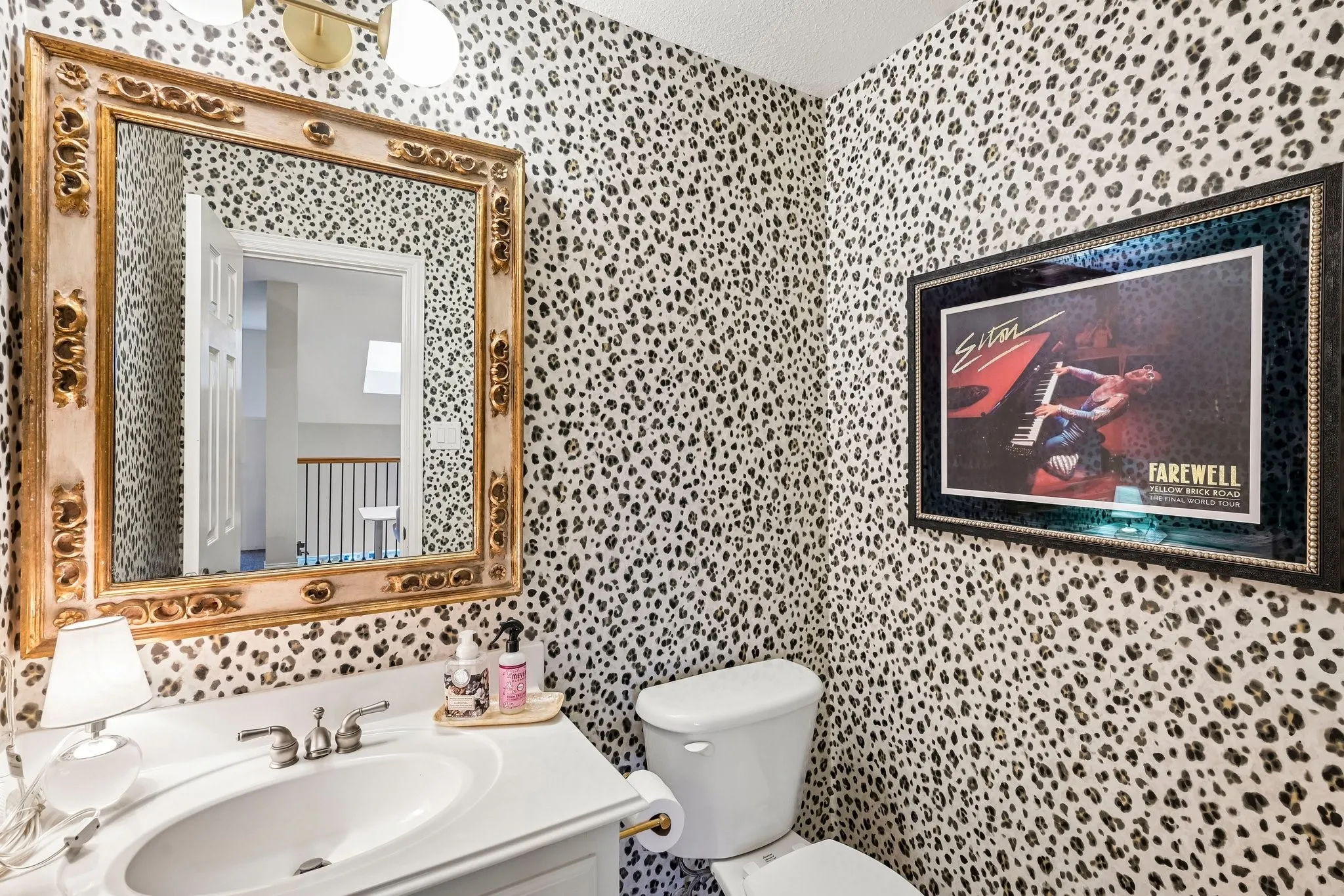 Powder room featuring leopard print wallpaper, a white vanity with an undermount sink, and a gold-framed mirror