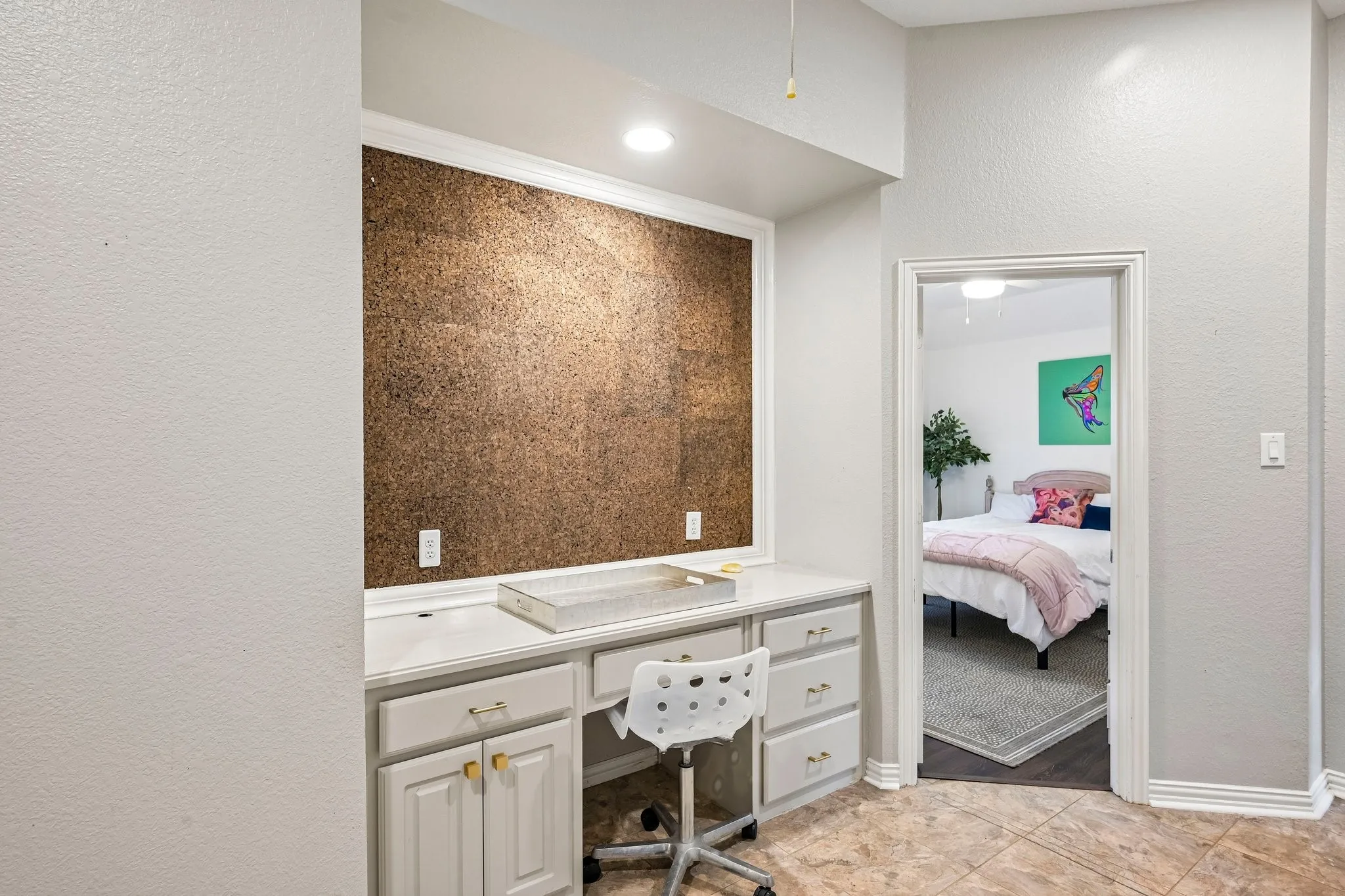 Built-in desk area featuring a cork accent wall, recessed lighting, and integrated cabinetry with gold-tone hardware