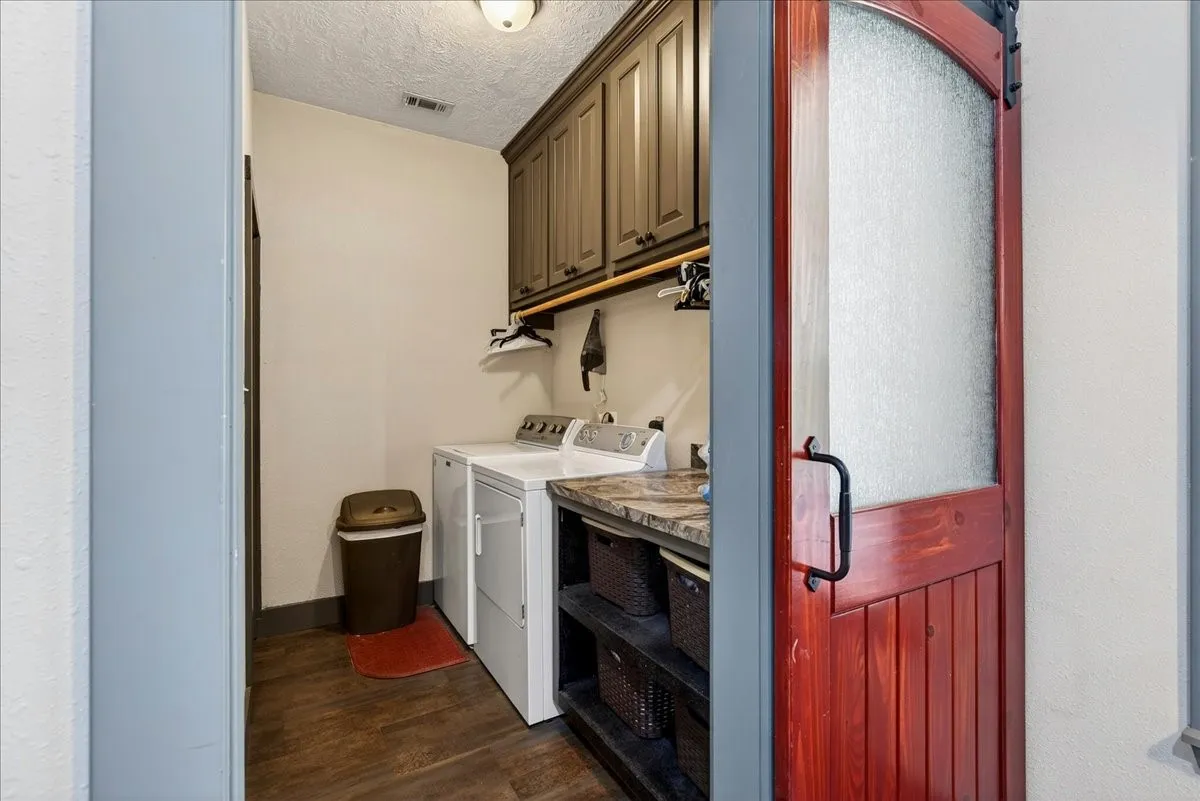 Laundry area featuring a rustic wood-finish barn door with frosted glass, wood-finish flooring, built-in upper cabinetry, and a stone-finish countertop with open shelving below. SPECIAL FEATURE: staircase leading down to the basement is in the most PERFECT out-of-the-way place - right here in the laundry room.