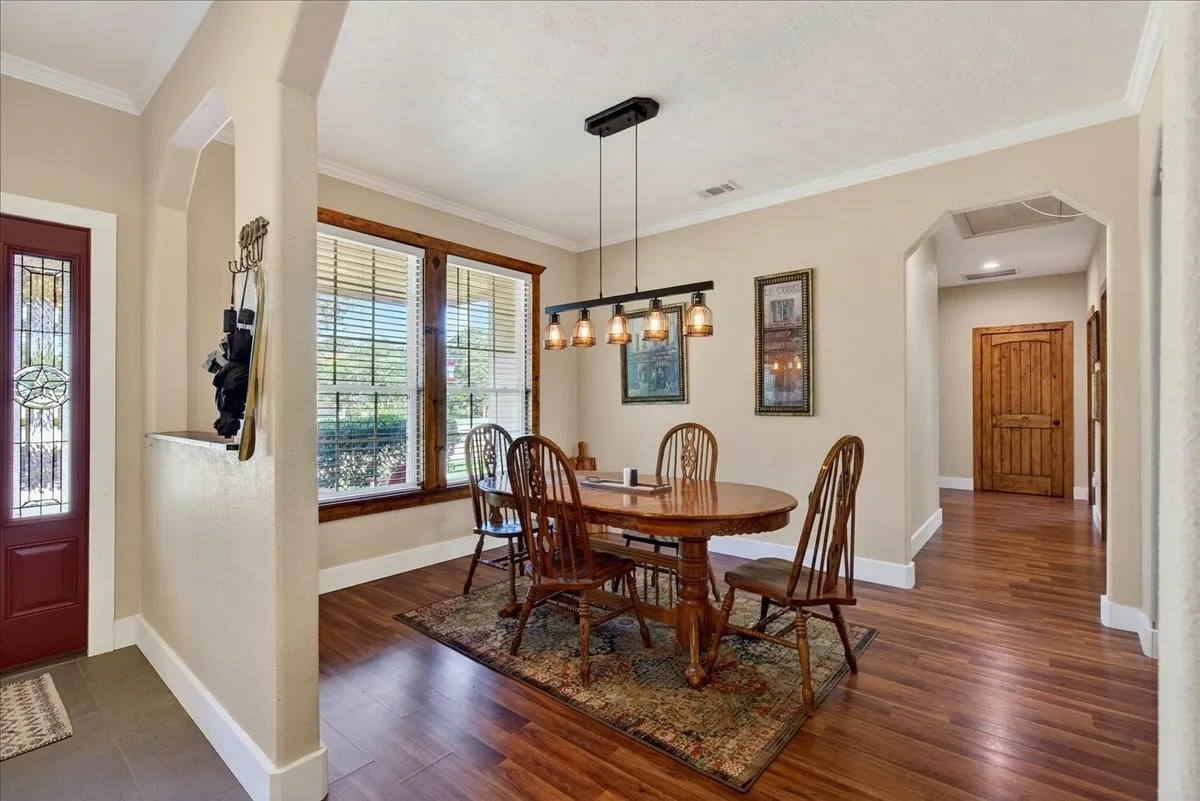 Dining area featuring wood-finish flooring, a linear chandelier, and expansive windows with wooden trim, open to the living-office-kitchen.