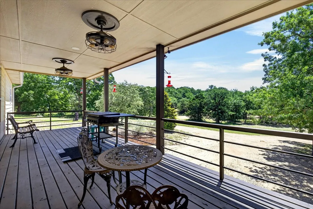 Spacious covered back porch deck featuring wood-finish decking, dark metal railings, and two industrial-style ceiling fans; so much space for family and friends to enjoy the peaceful serenity of country living.