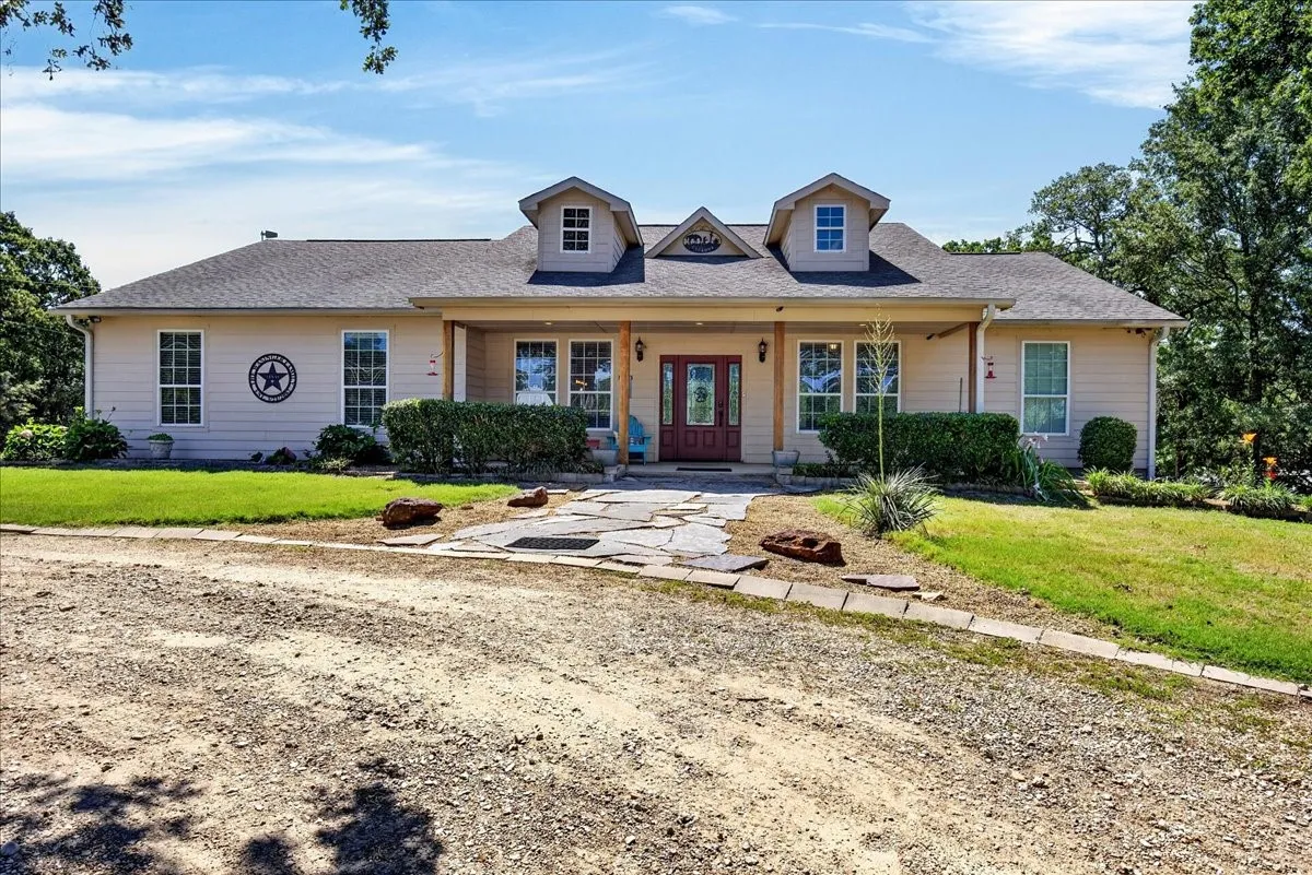 Ranch-style residence featuring a covered front porch with natural wood columns, a red entry door, multiple dormer windows, and a flagstone pathway