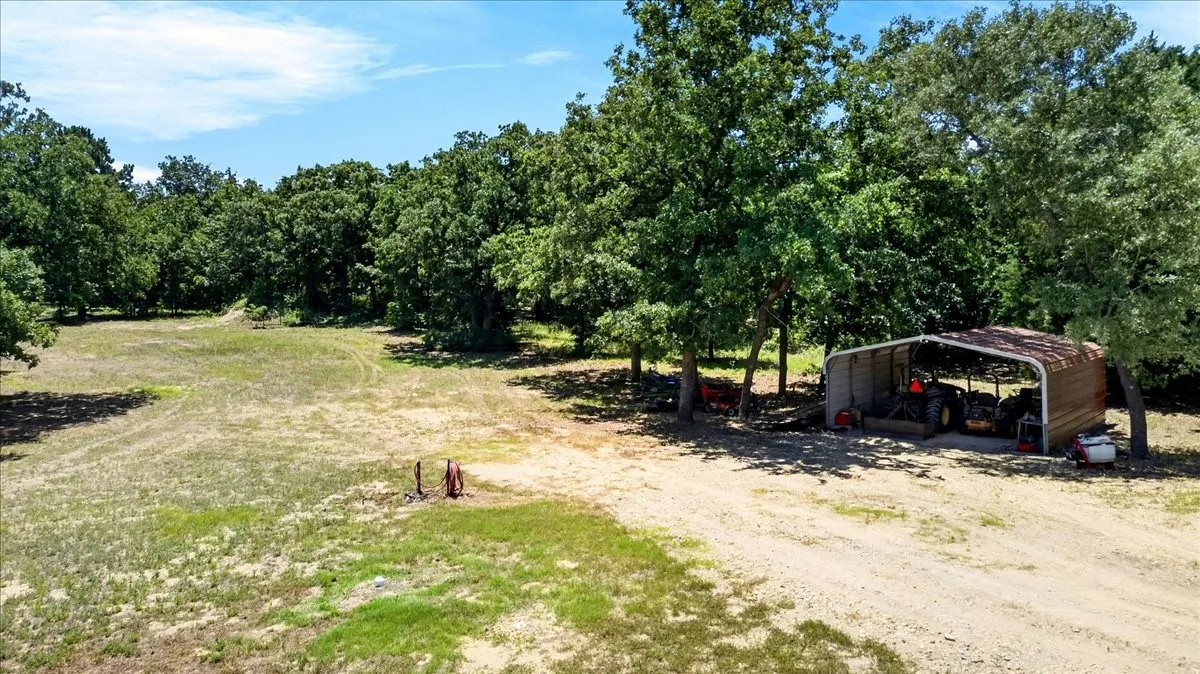 Expansive clearing surrounded by mature trees, featuring a gravel driveway and a 2-car carport.
