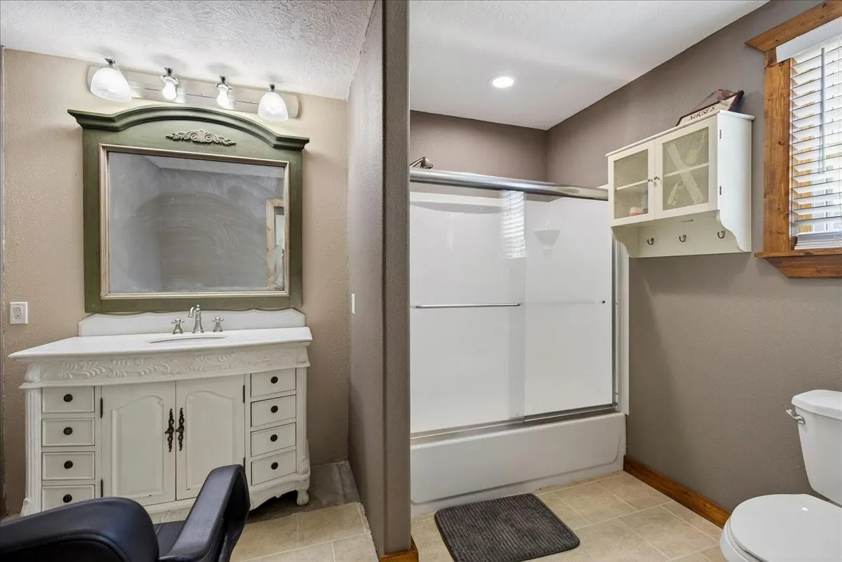 4th Bathroom in Basement Level 2 featuring a decorative vanity with an integrated sink, a large framed mirror, and a shower-tub combination with a sliding glass door.  Next door to this room is a Utility Room.