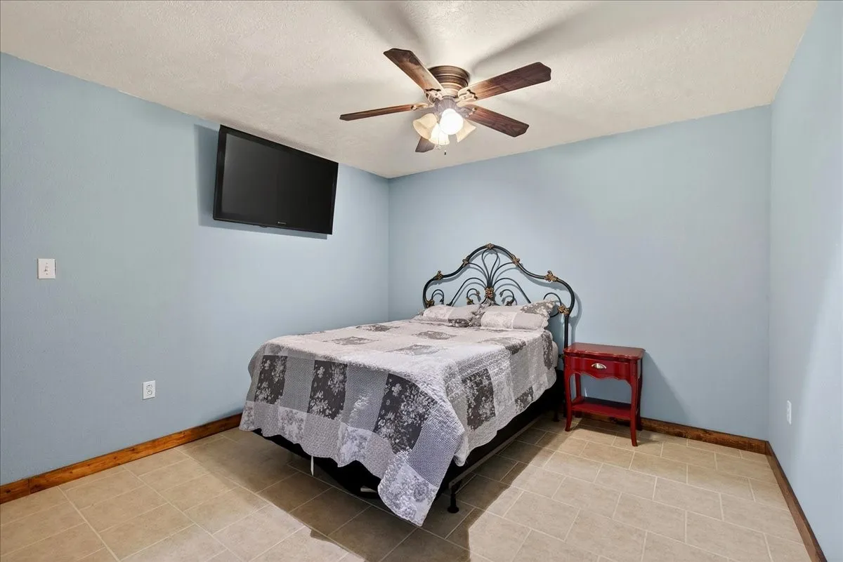 5th Bedroom in Basement level with Light blue painted walls featuring a ceiling fan with light fixture and tile flooring and closet.  SPECIAL FEATURE: this room is also an EMERGENCY SAFE ROOM because of the completely concreted walls and no window.