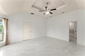 Spacious interior room featuring a tray ceiling with a ceiling fan, large format tile flooring, and vaulted ceiling details