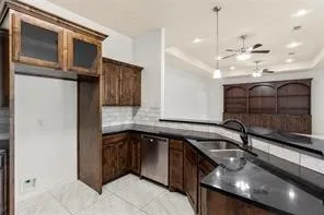 Modern kitchen featuring dark wood cabinetry, stainless steel dishwasher, black countertops, and a white subway tile backsplash