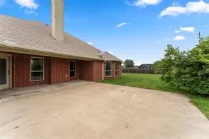Brick exterior with a gabled shingle roof, featuring a concrete patio, multiple windows, and an expansive grass​​‌​​​​‌​​‌‌​‌‌​​​‌‌​‌​‌​‌​​​‌​​ lawn