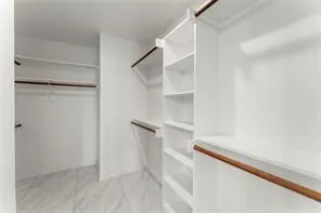 Spacious walk-in closet featuring white built-in shelving, multiple hanging rods, and light-toned tile flooring
