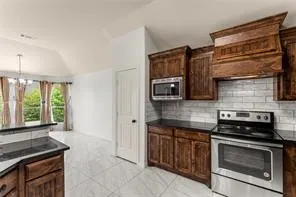 Kitchen featuring dark wood cabinetry, stainless steel appliances, a subway tile backsplash, and dark countertops