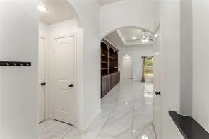 White walls frame a hallway featuring large format tile flooring and a built-in wood-finish bookcase