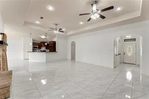 Spacious living area featuring large format tile flooring, a tray ceiling with recessed lighting, and ceiling fans