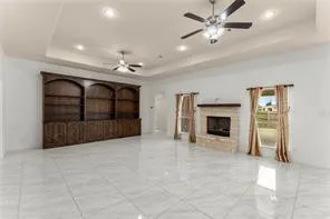Spacious living area featuring polished tile flooring, a built-in wood cabinetry unit, and a stone fireplace