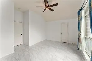 Spacious room featuring vaulted ceilings, a ceiling fan with integrated lighting, two panel interior doors, and large format tile flooring