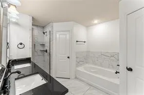 Full bathroom featuring a dark countertop vanity with an undermount sink, a tiled walk-in shower with shelving, and a separate bathtub with tile surround