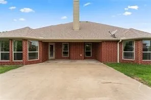 Brick exterior featuring a concrete patio, multiple windows, and a shingle roof