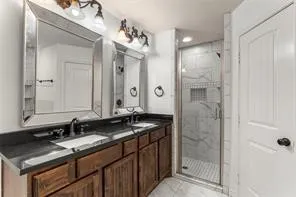 Dual sink vanity with dark wood-finish cabinetry, black countertop, and undermount sinks