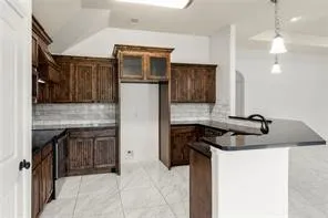 Kitchen featuring dark wood cabinetry, a tiled backsplash, and black countertops