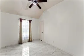 Room featuring a vaulted ceiling with a ceiling fan, a large window, tiled flooring, and a solid interior door