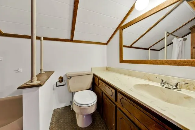 Vaulted ceiling with exposed wood beams, extended vanity with integrated sink, wood cabinetry, and hexagonal floor tiling
