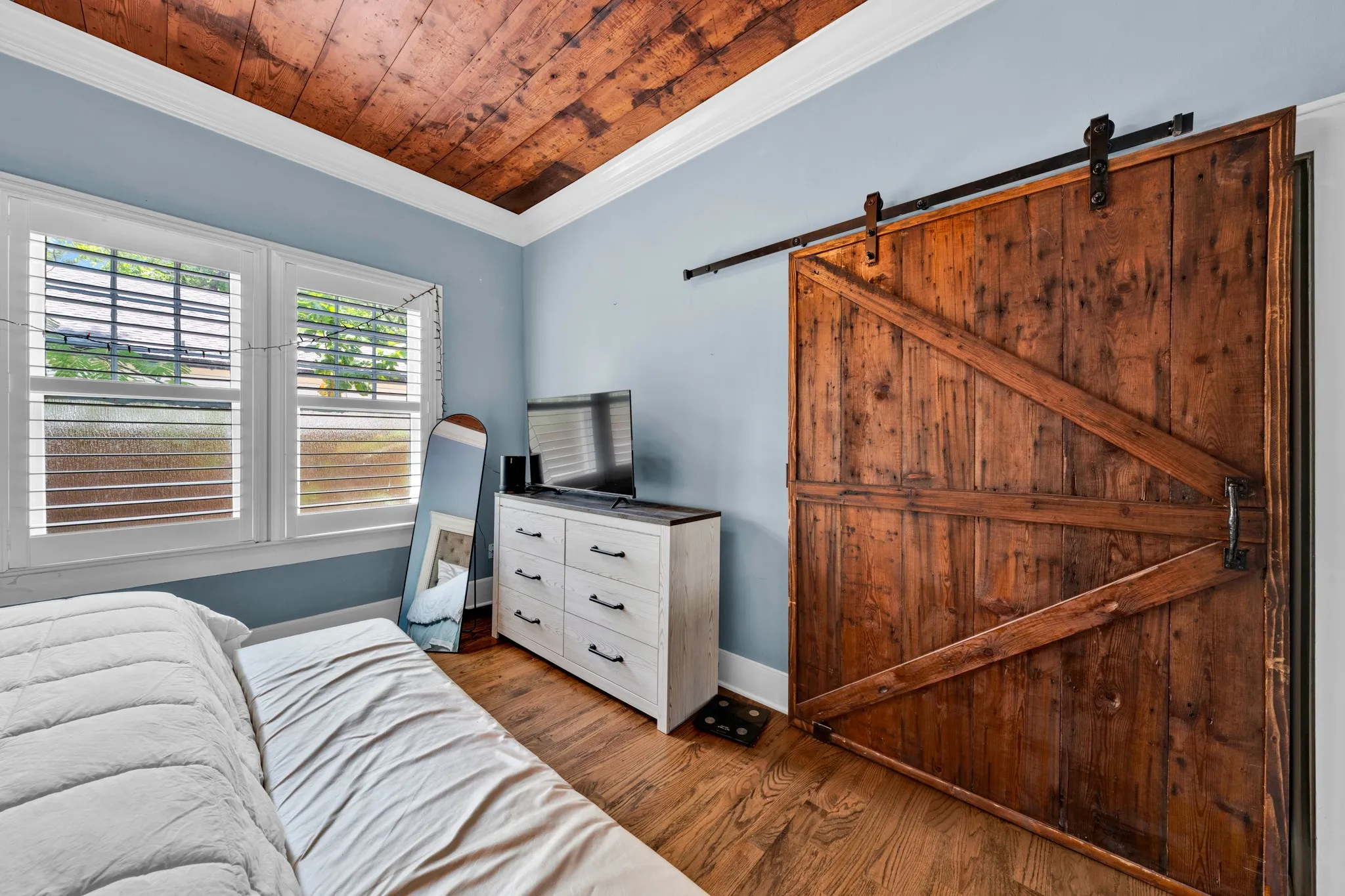 Wood-plank ceiling, wood-finish flooring, white window shutters, and a sliding barn door with black hardware