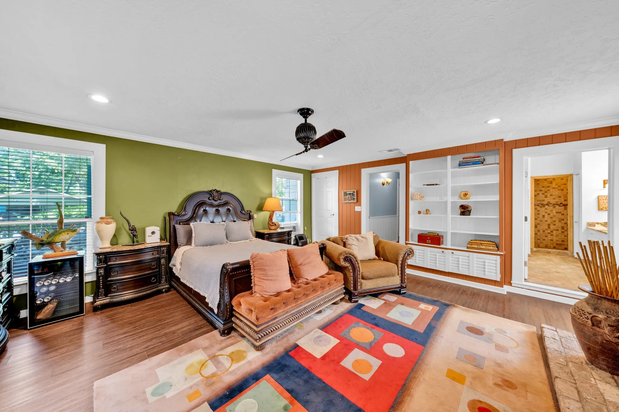 Primary bedroom suite featuring hardwood flooring, a ceiling fan with integrated lighting, and custom built-in cabinetry with glass-front display shelving