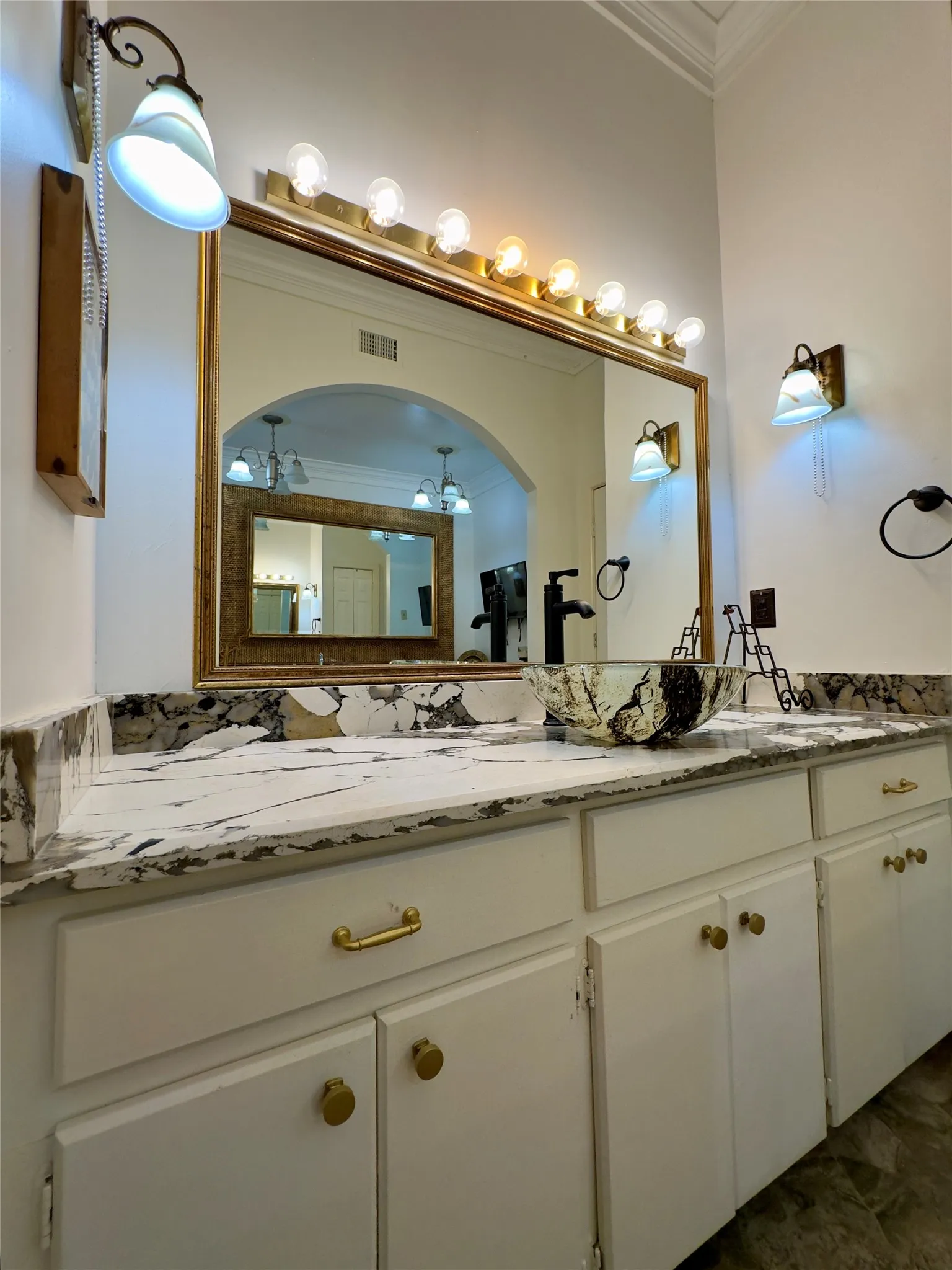 Double vanity with white cabinetry and gold-toned hardware, featuring a vessel sink and a large framed mirror with integrated lighting