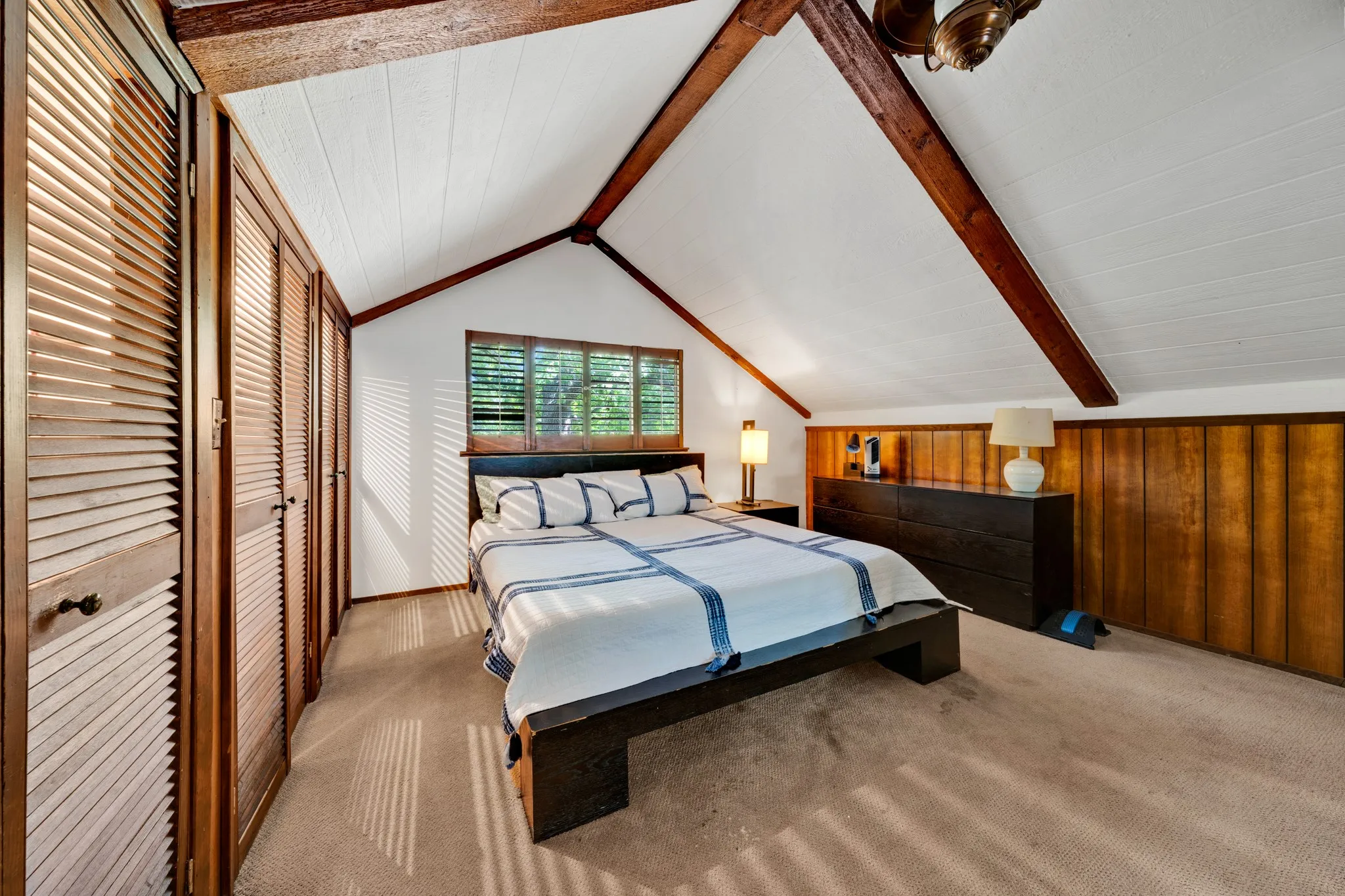 Vaulted ceiling with exposed wood beams, wall-to-wall carpeting, wood-paneled walls, and louvered closet doors