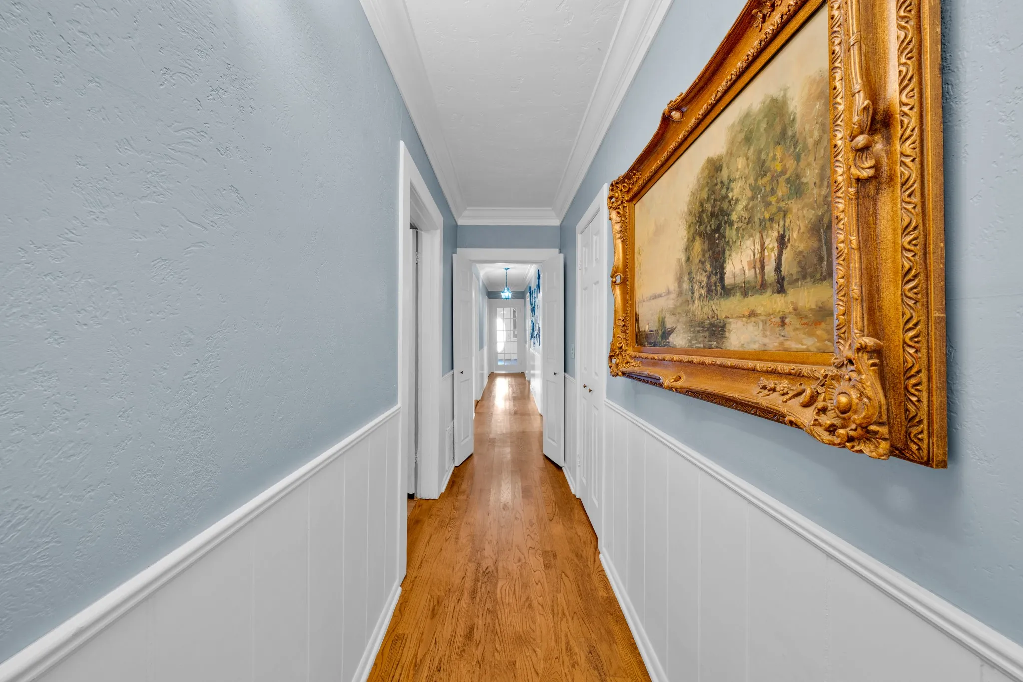 Hallway featuring wood-finish flooring, white wainscoting, textured walls, and crown molding