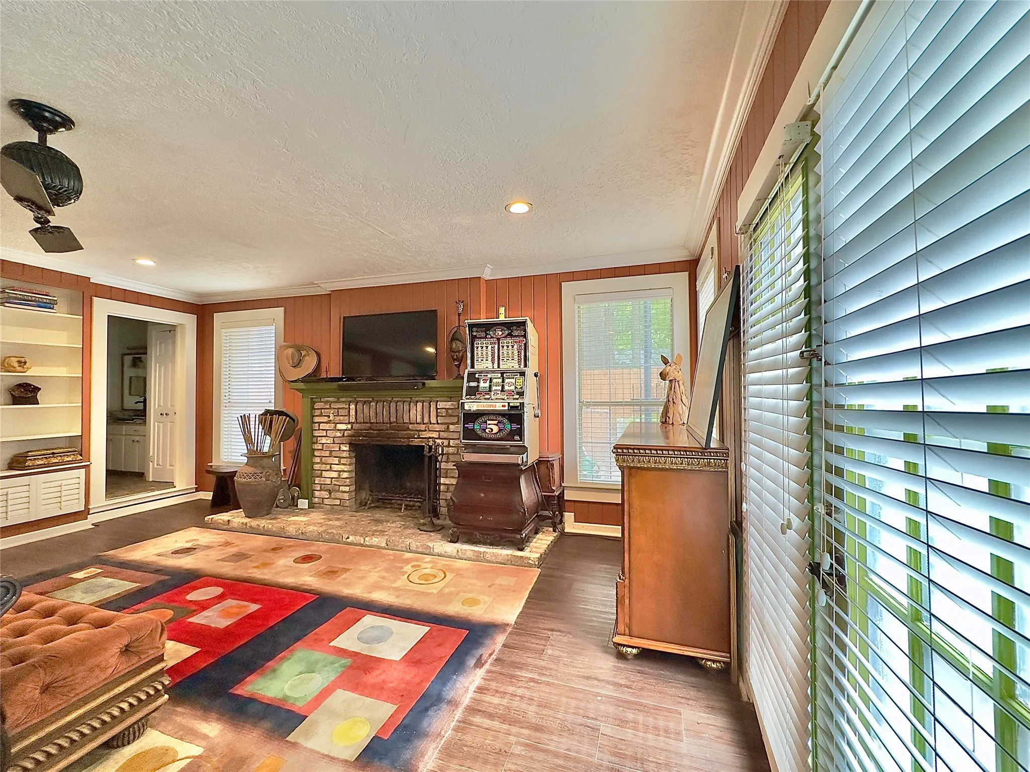 Brick-faced fireplace with a painted mantel, wood-finish flooring, built-in shelving, and a ceiling fan