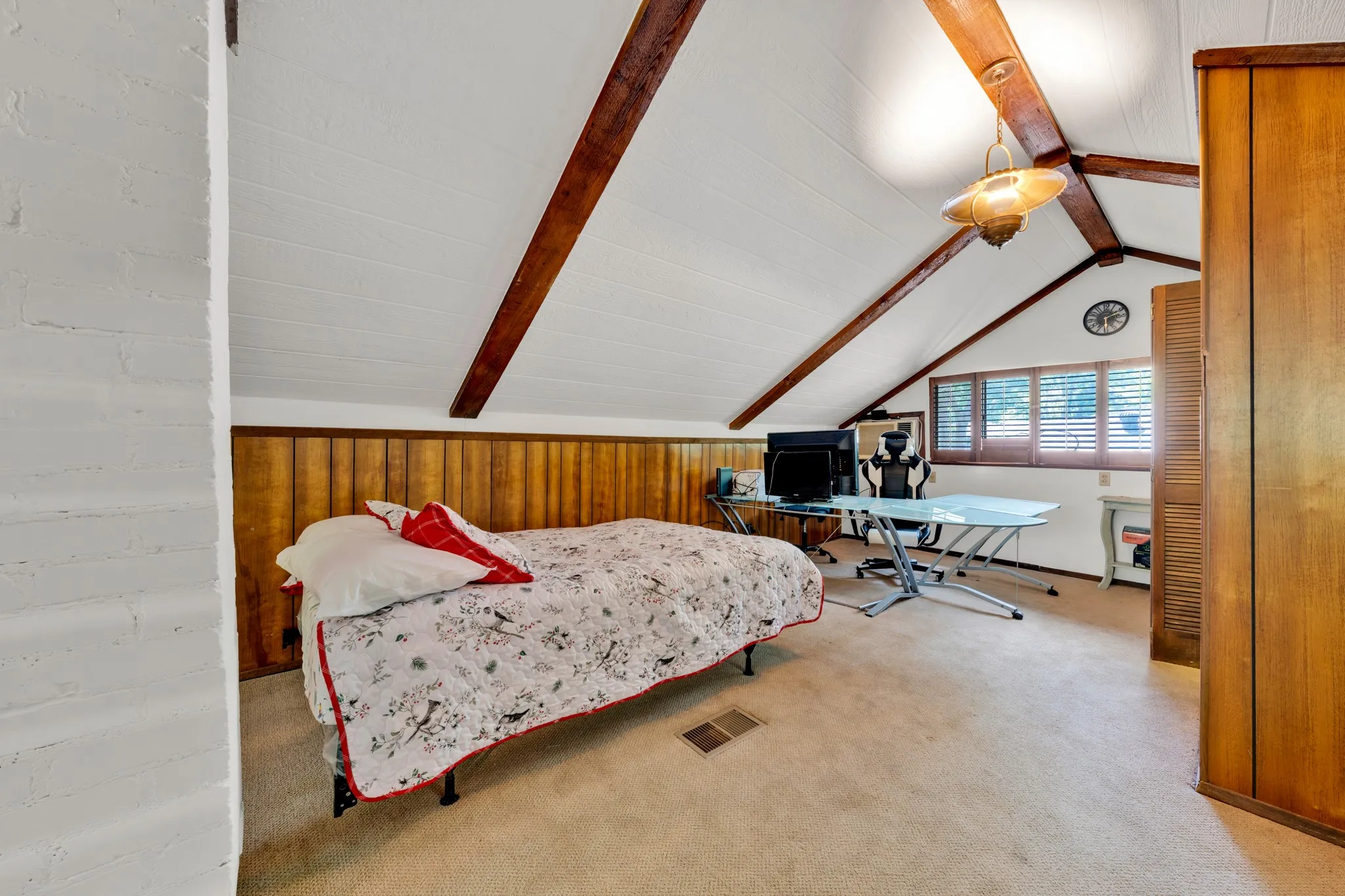 Vaulted ceiling with exposed wood beams, wood-paneled wainscoting, wood-frame windows with interior shutters, wall-to-wall carpeting, and a built-in wood wardrobe