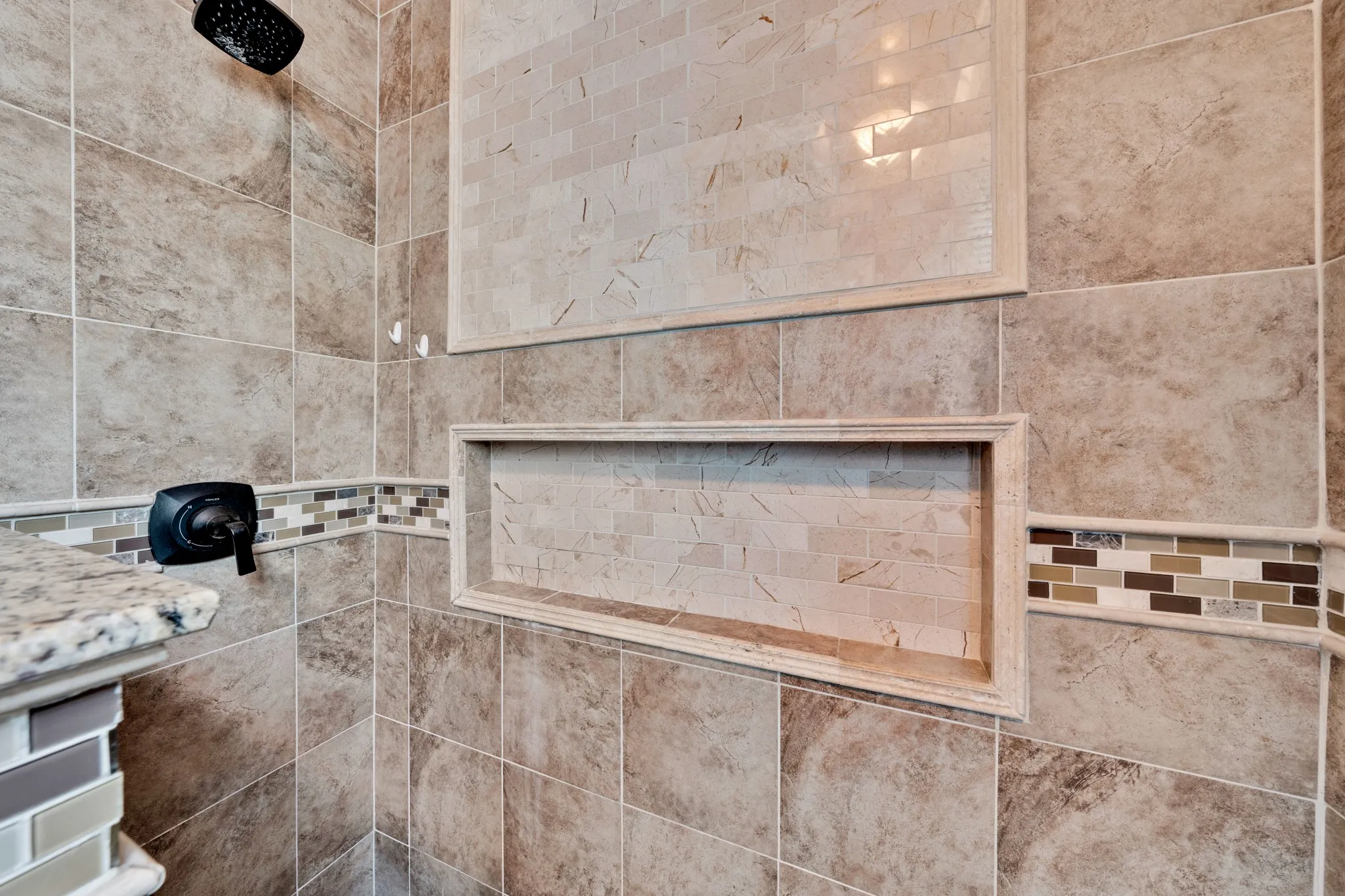 Tiled shower with a rainfall shower head, built-in niches, and a decorative mosaic border