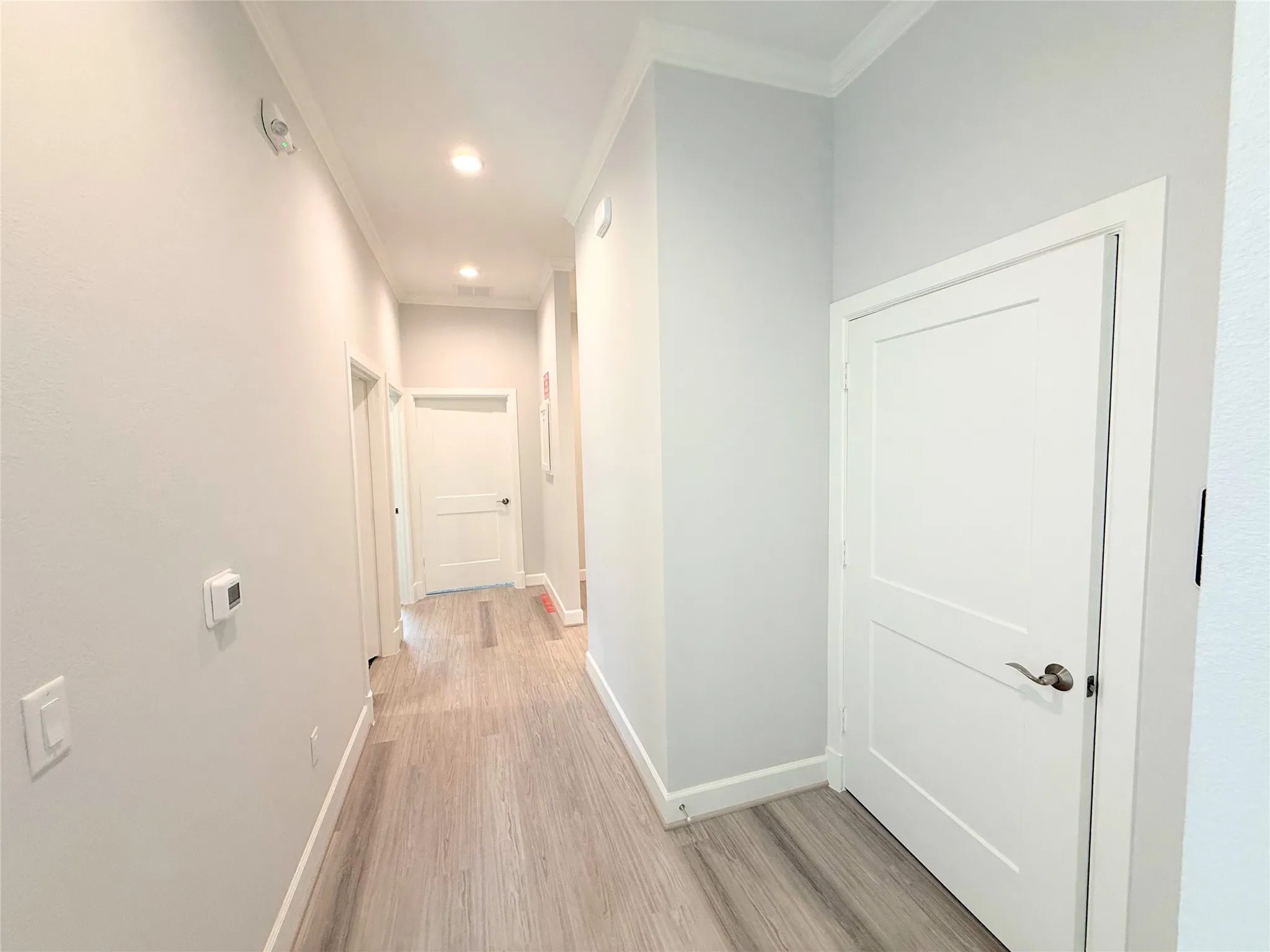 Hallway featuring wood-finish flooring, recessed lighting, crown molding, two-panel interior doors, and modern wall-mounted thermostat