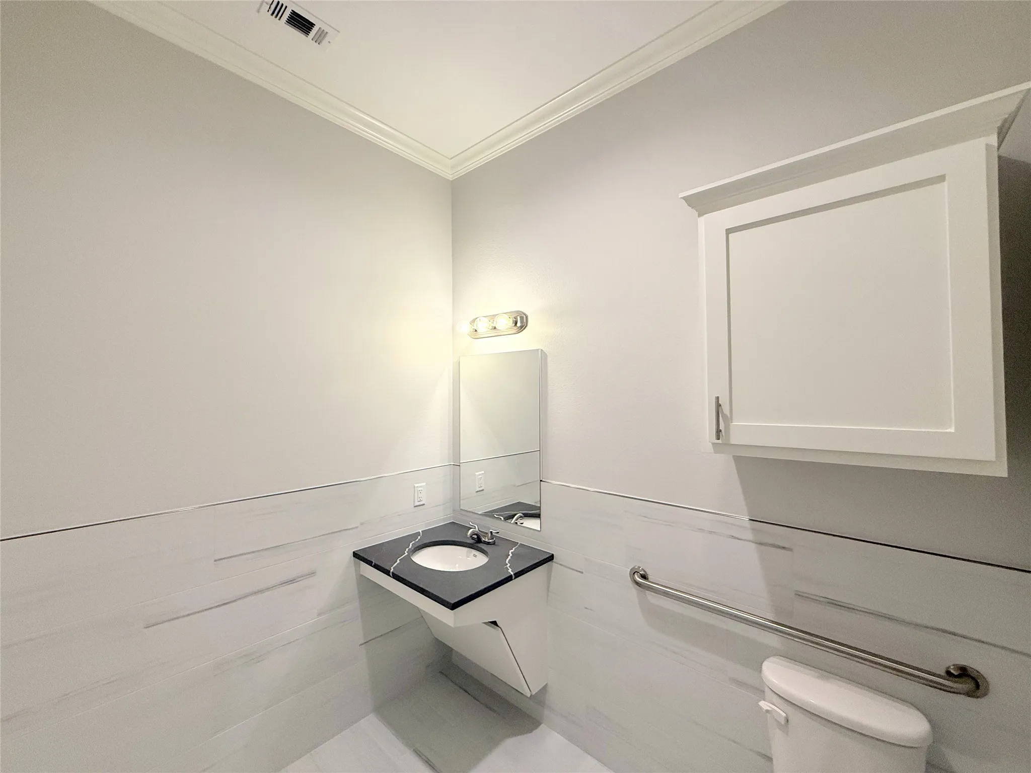 Bathroom featuring a wall-mounted vanity with a black countertop and integrated sink, white wall-mounted cabinet, vanity lighting, and wall-mounted grab bar