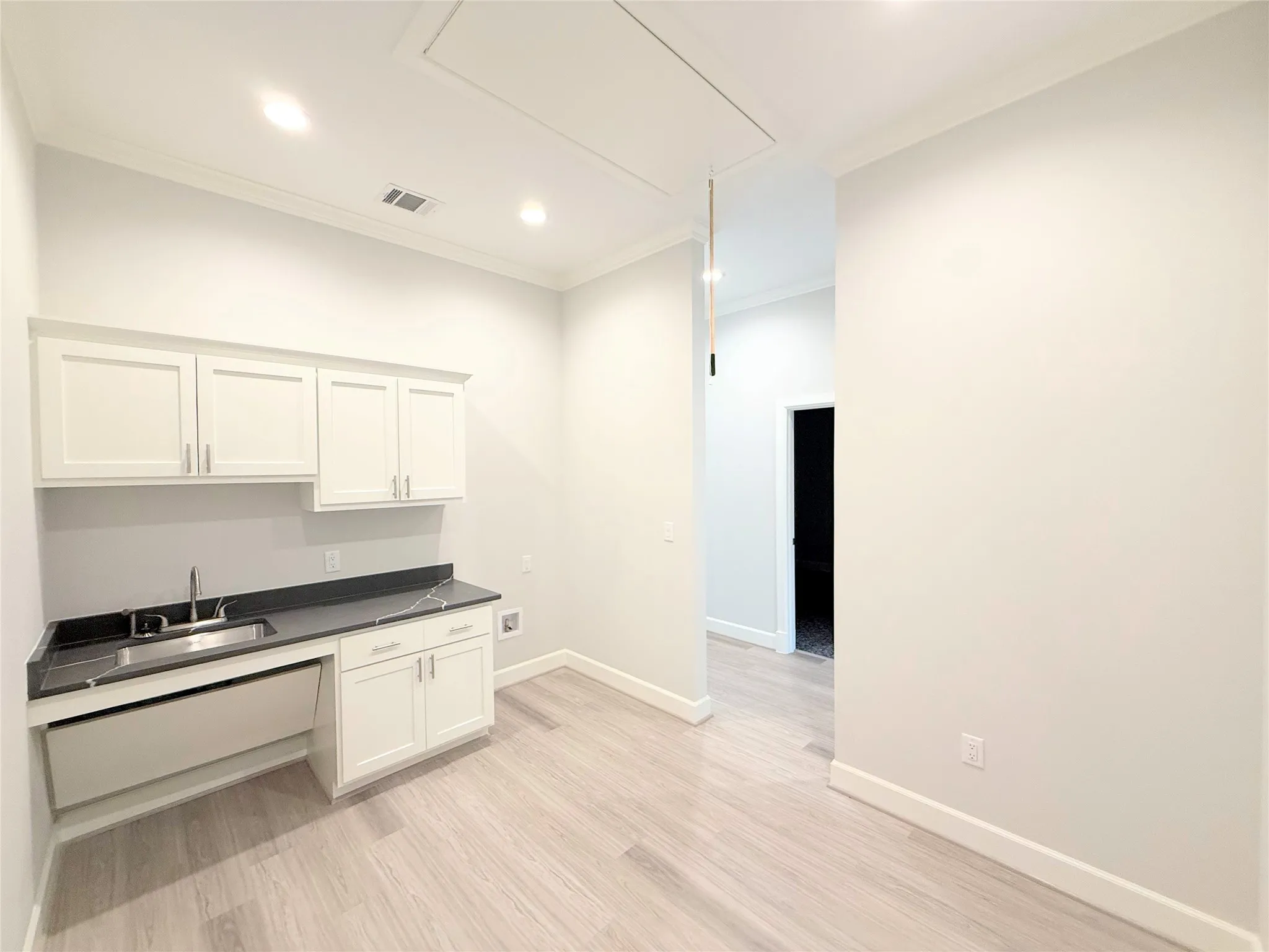 Utility area featuring a stainless steel sink, dark countertop, and white shaker-style cabinetry
